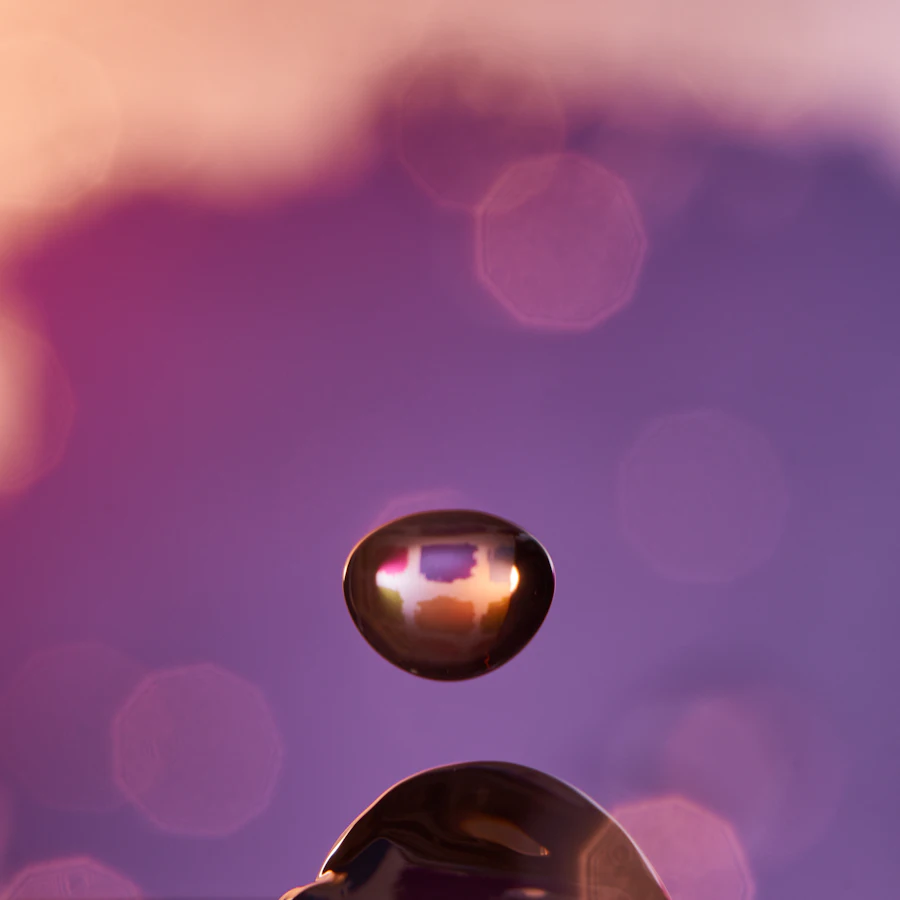 A water droplet suspended against a warm rose-and-lilac glow