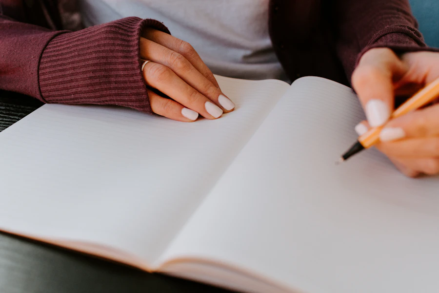 Hands writing in an open notebook at a desk in soft light